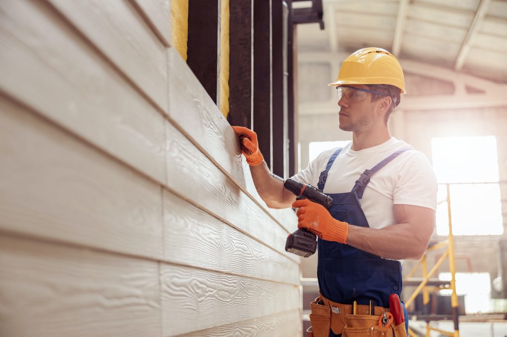 Handsome young man builder installing exterior wood siding